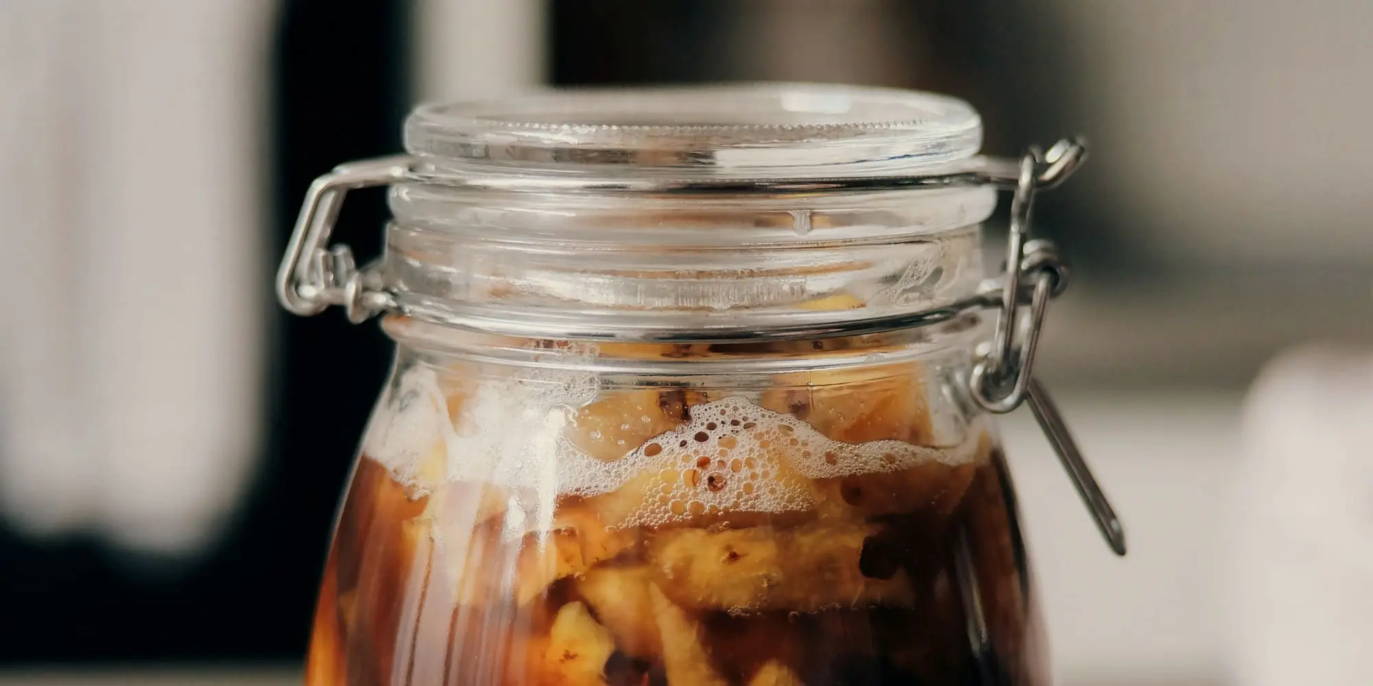 A glass jar of vegetables bubbling in a brown brine