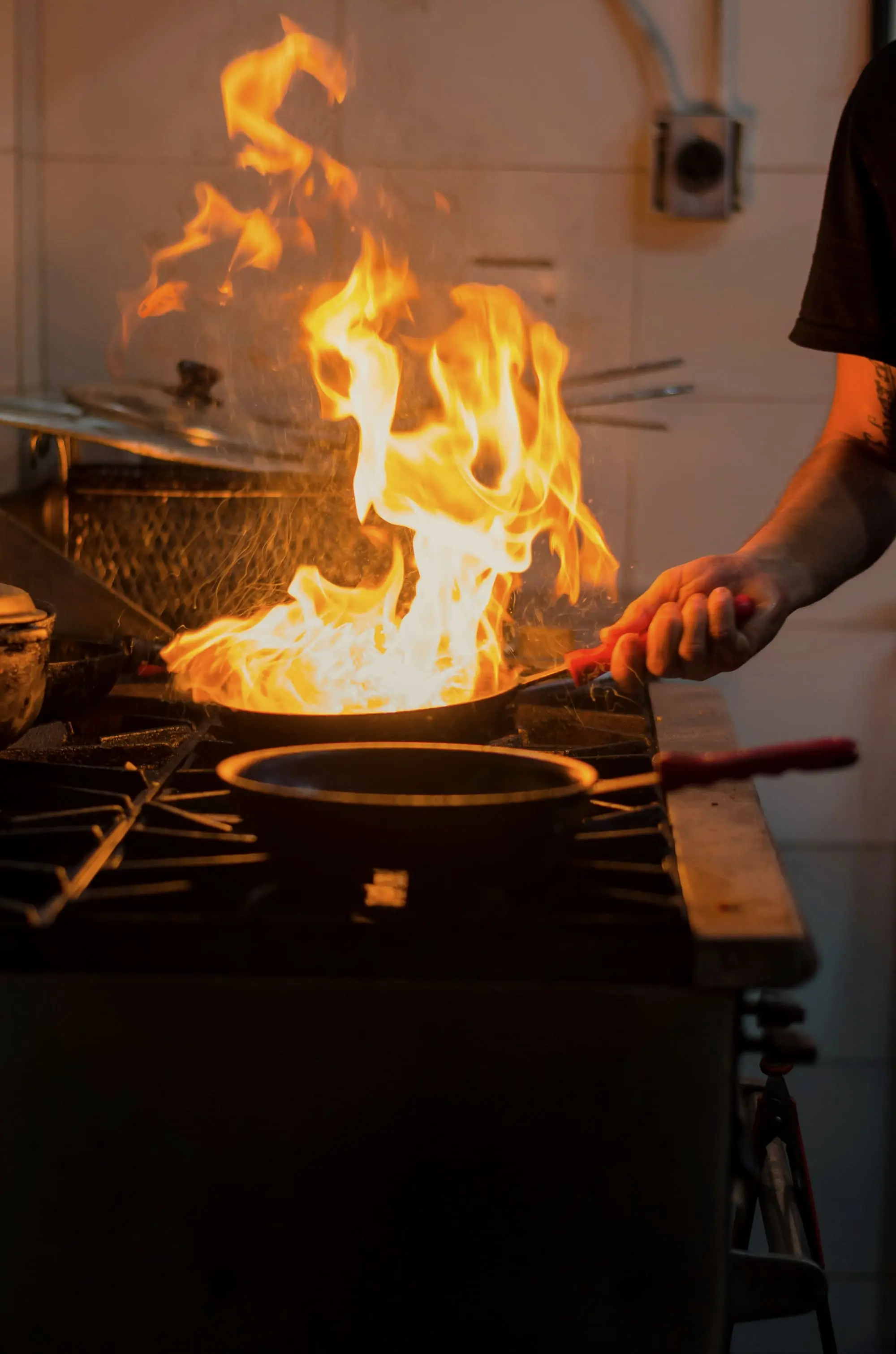 A cook’s hand tipping a pan, flames leaping from it