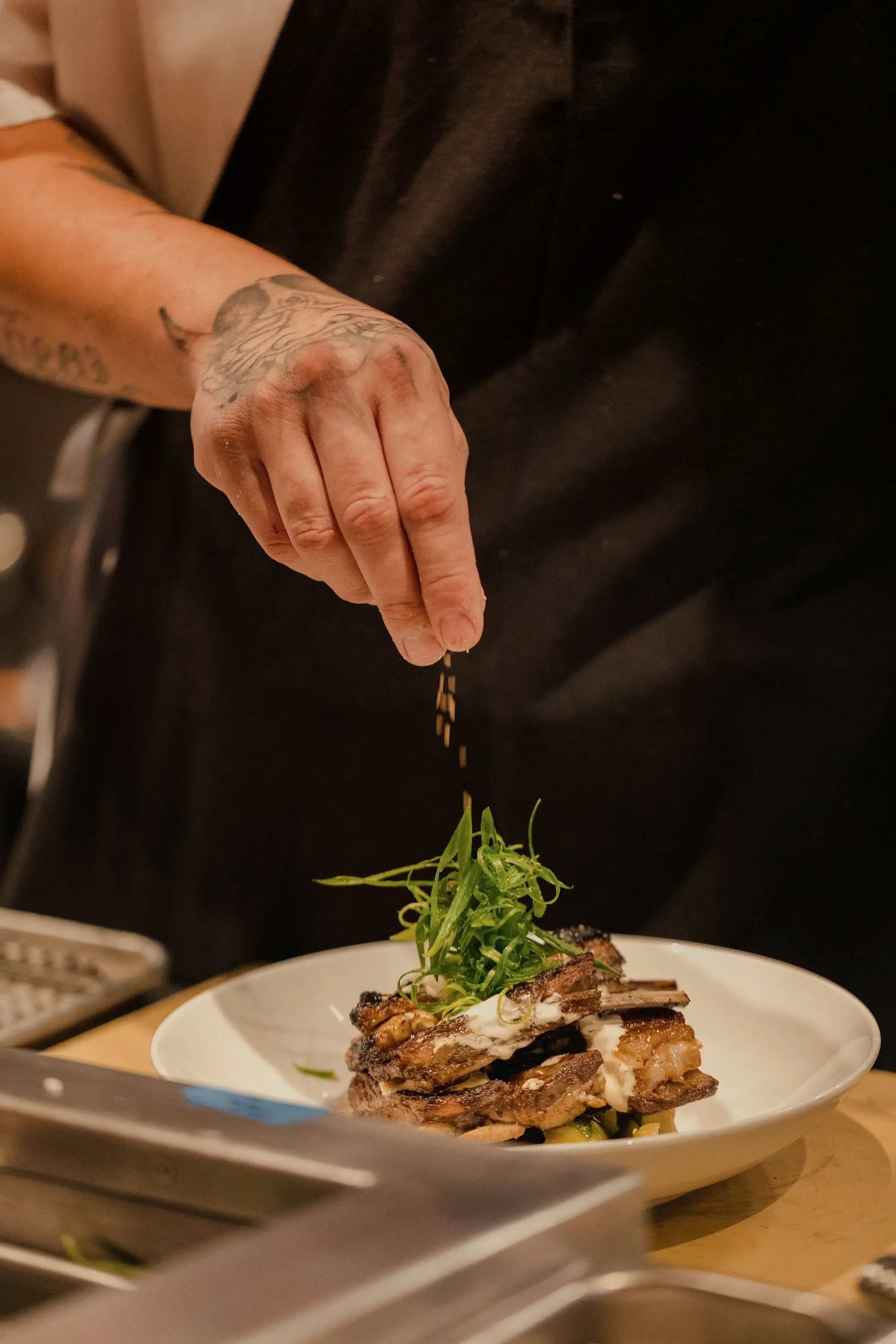 Fingers scattering seasoning over a plate crowned with fresh herbs