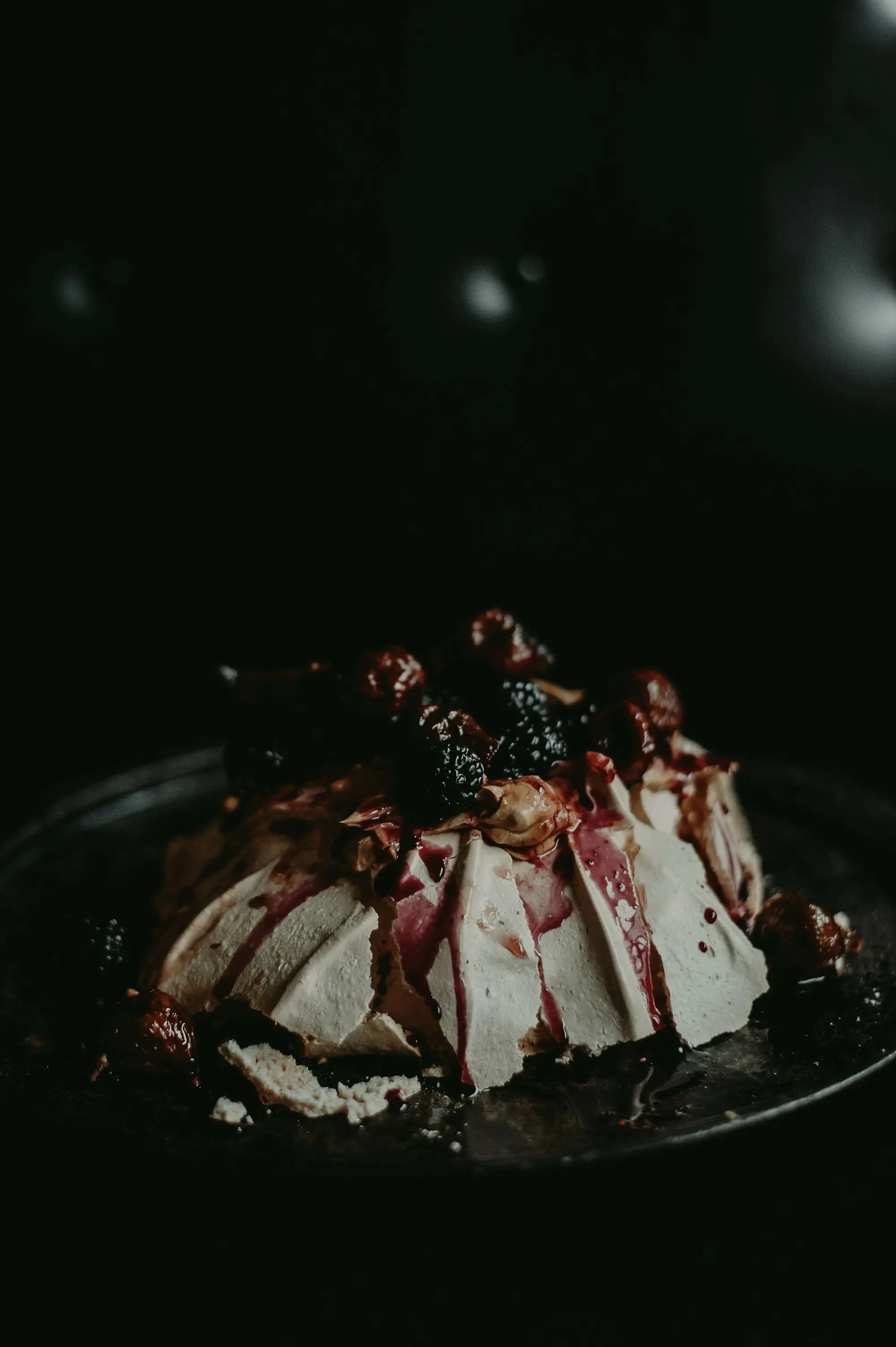 Meringue dessert dressed in blackberries and a dark berry syrup on a black plate