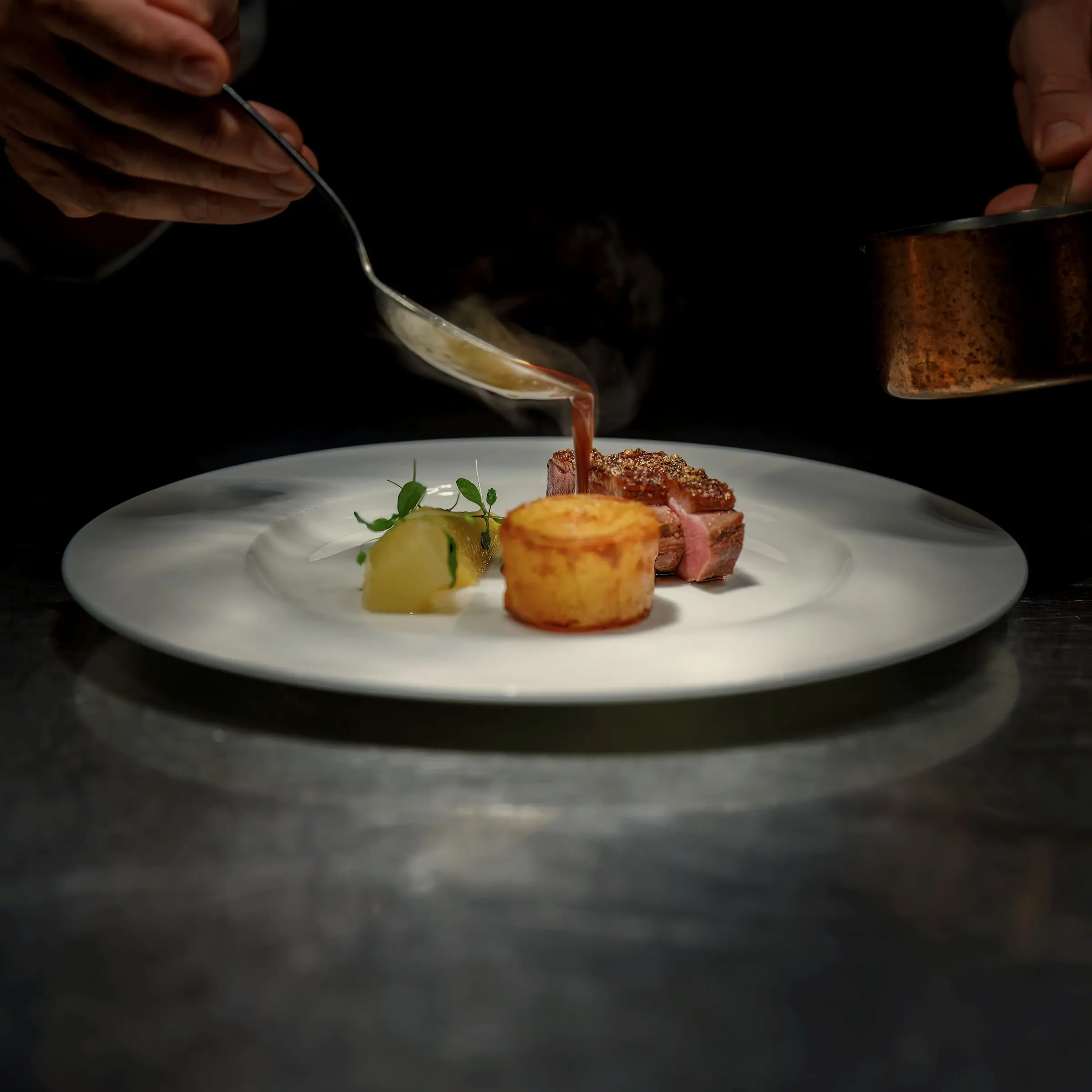 Sauce spooned over a plate of seared meat and potato on a grey stone counter