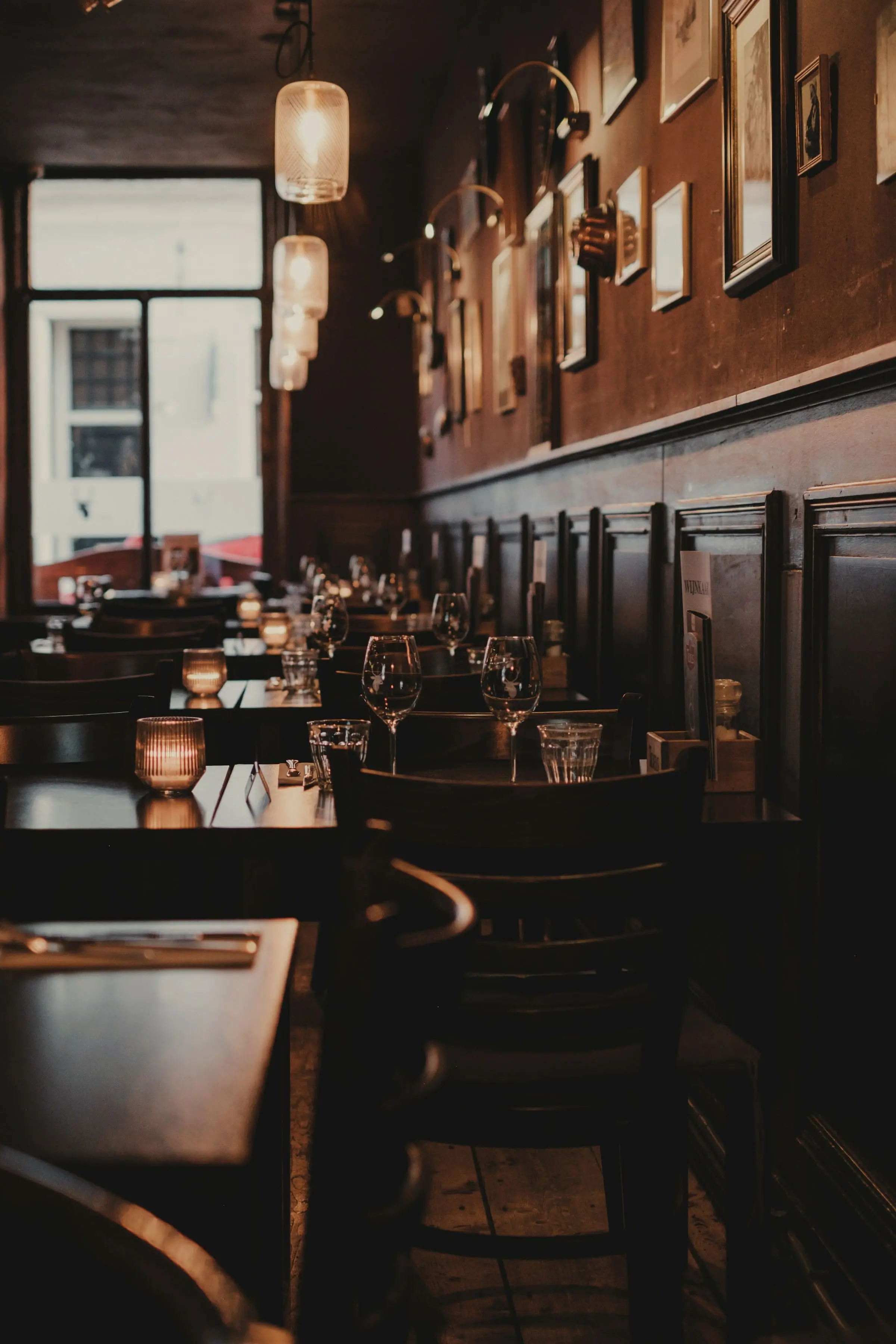 A dark-panelled dining room, tables laid with glasses and candles