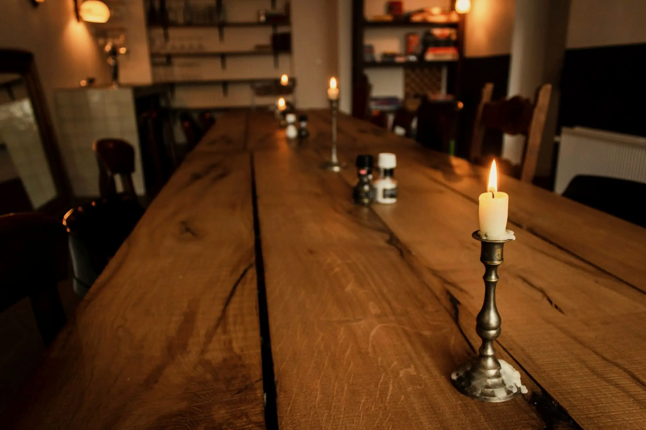A long oak table with a lit candle on a brass holder